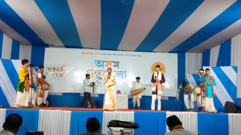 A girl singing at centre stage with a Bihu band