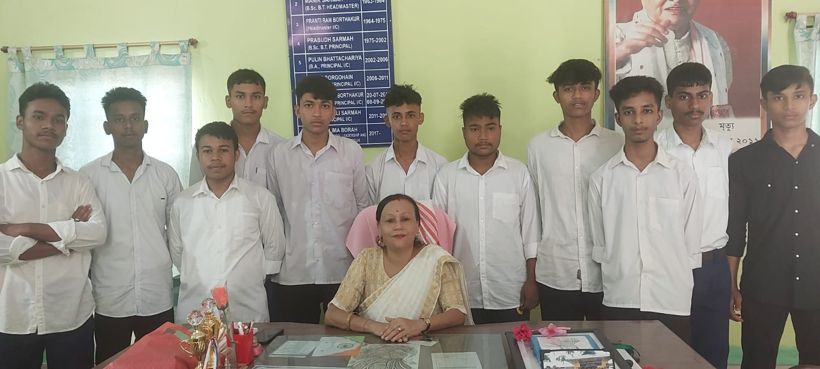 Shyamalima Borah seated at her desk with senior students standing behind her